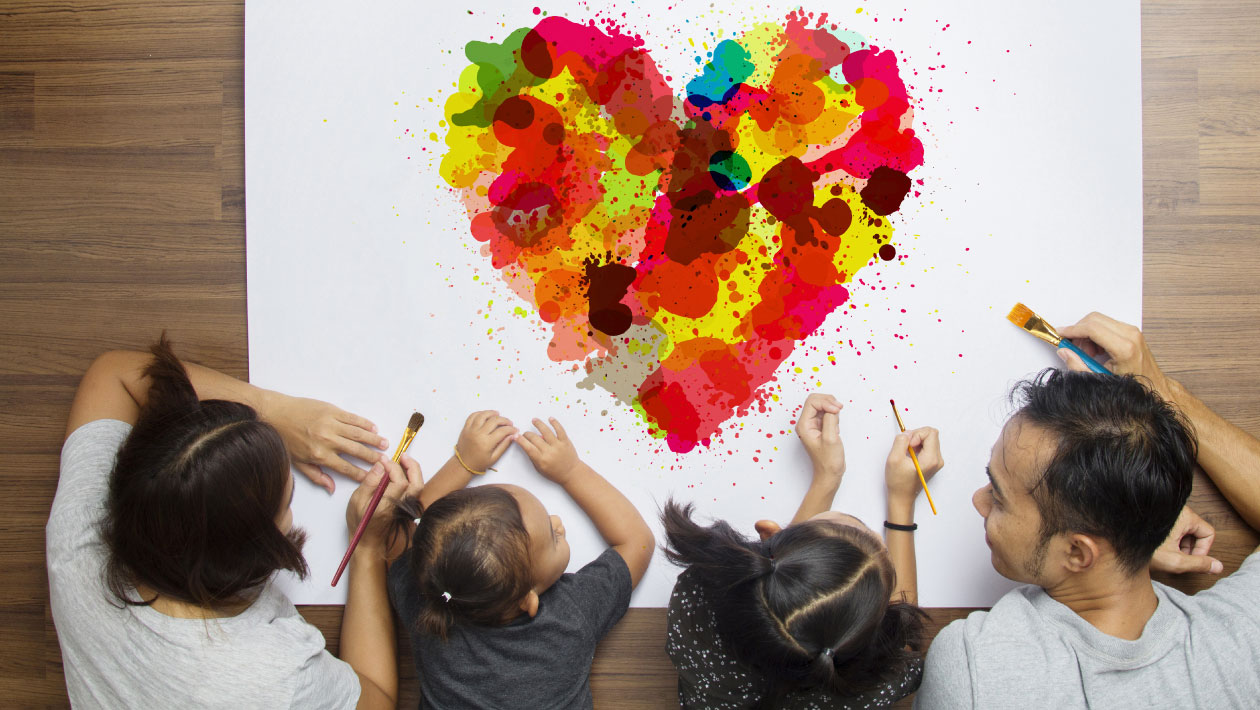 Kids sitting at a table with a Crayola Imagine Arts Academy art instructor drawing a multi colored heart using paint brushes 